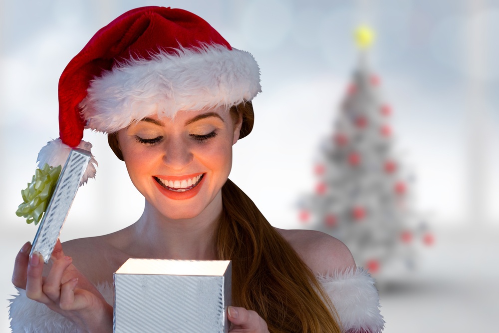 Sexy girl in santa costume opening a gift against blurry christmas tree in room