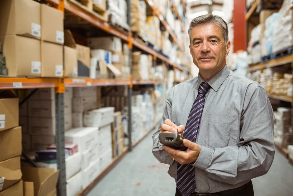 Smiling male manager using handheld in a large warehouse
